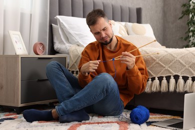 Man learning to knit with online course on floor at home