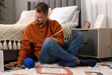 Man learning to knit with online course on floor at home