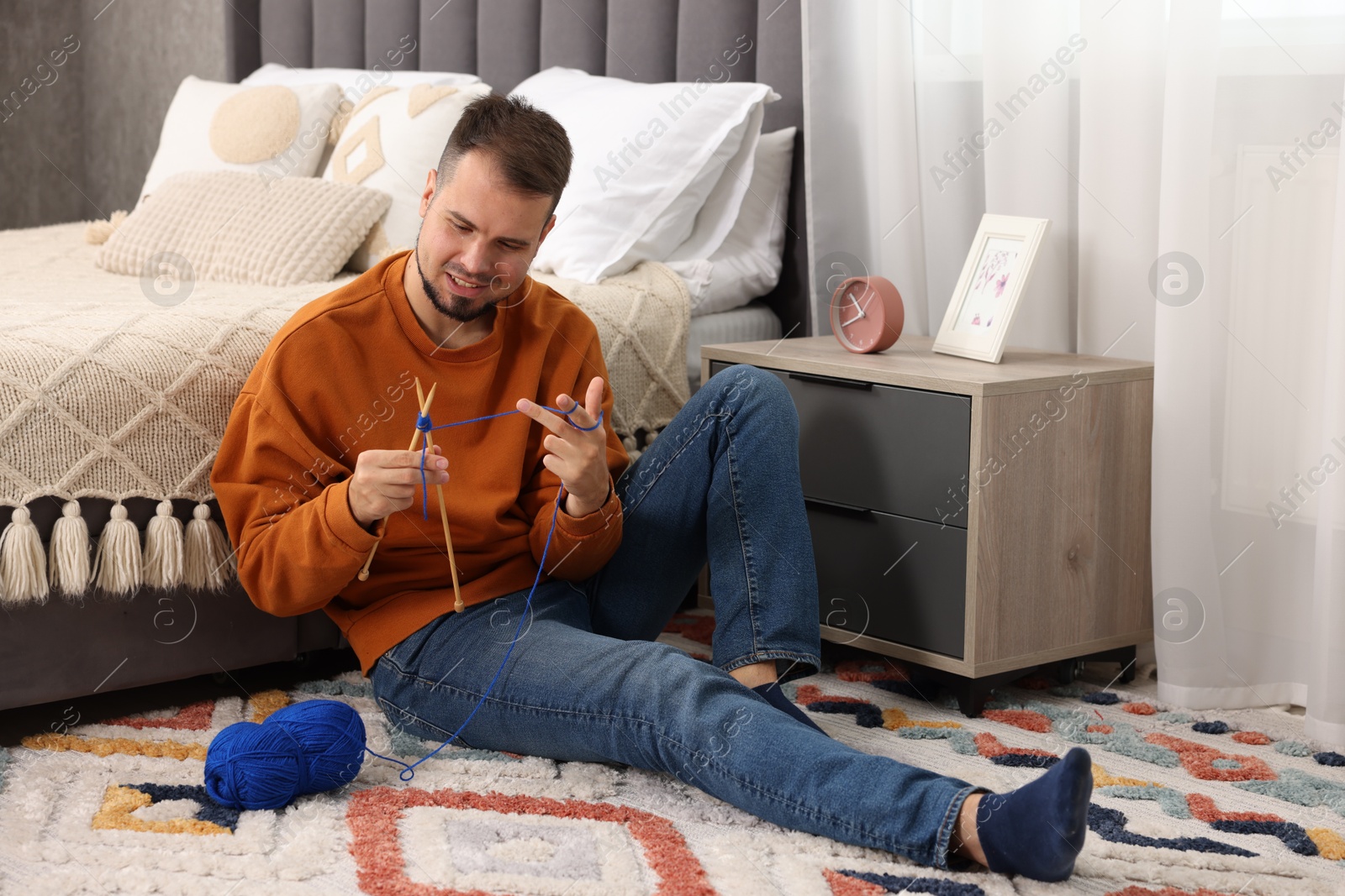 Photo of Man knitting with needles on floor at home