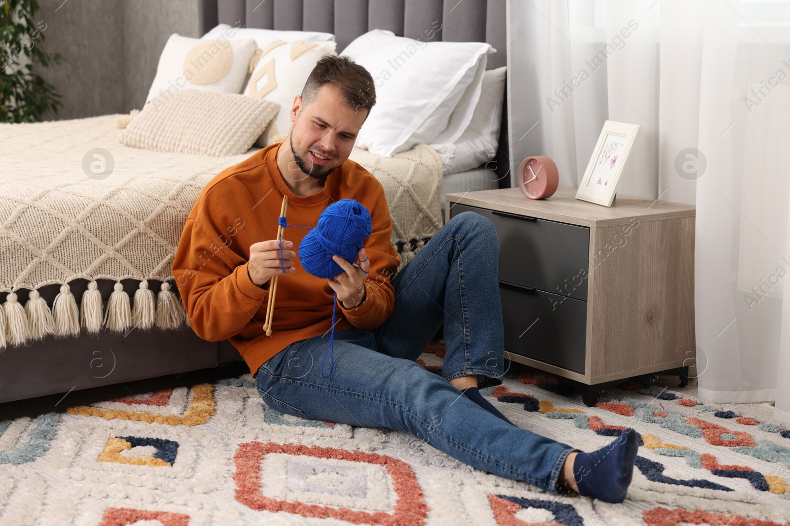 Photo of Man knitting with needles on floor at home