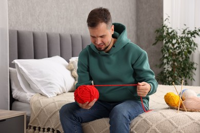 Man with red yarn on bed at home. Knitting material