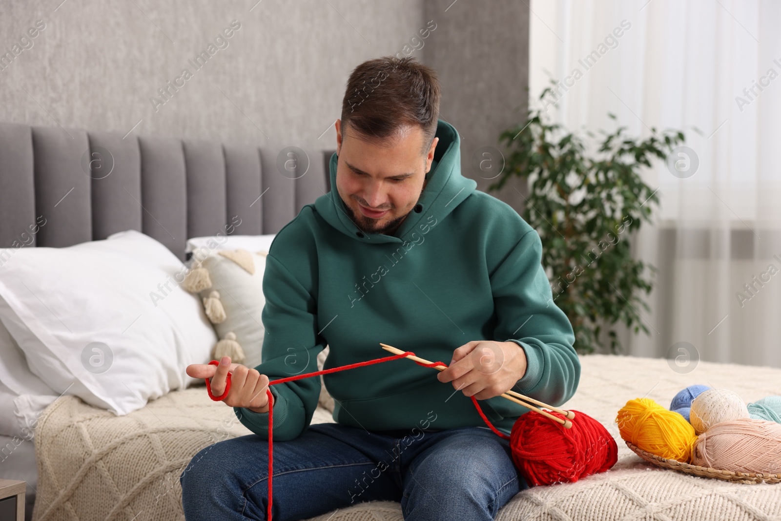 Photo of Man knitting with needles on bed at home