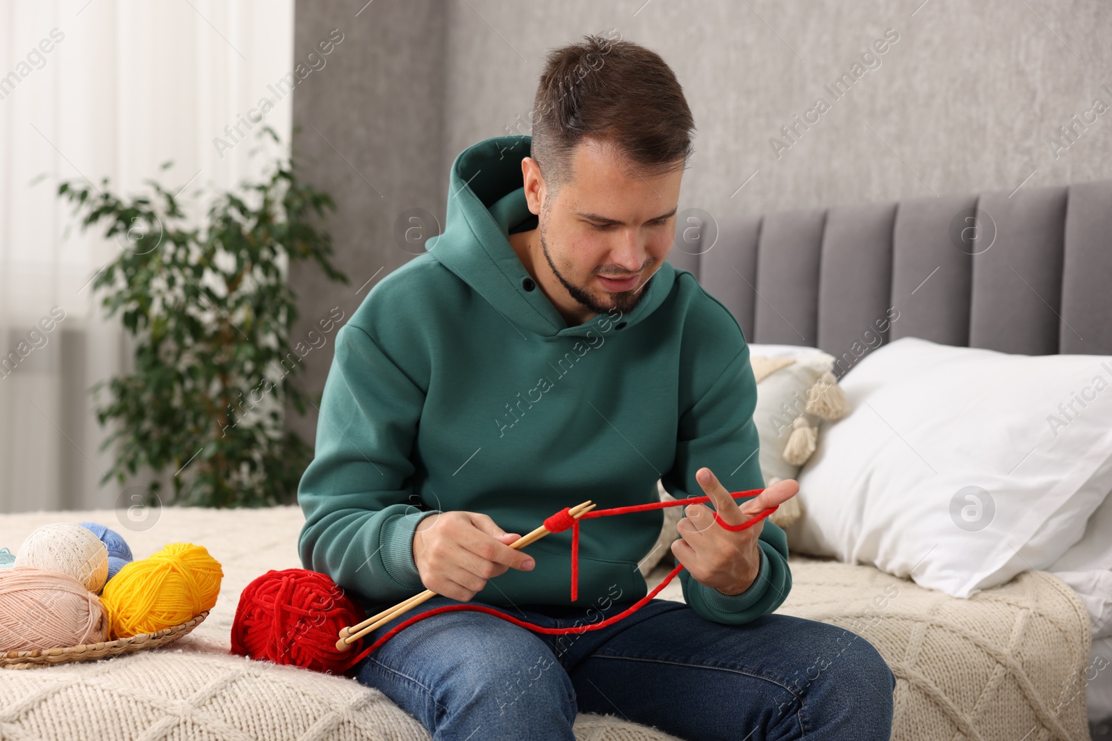 Photo of Man knitting with needles on bed at home