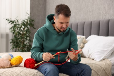 Photo of Man knitting with needles on bed at home