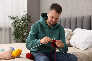 Man knitting with needles on bed at home