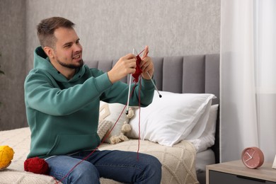 Photo of Man knitting with needles on bed at home