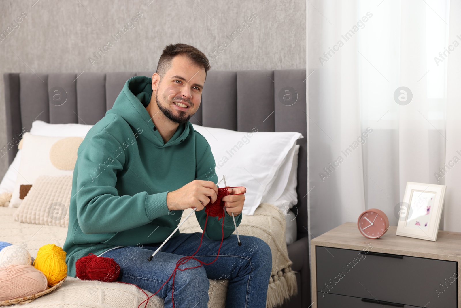 Photo of Man knitting with needles on bed at home