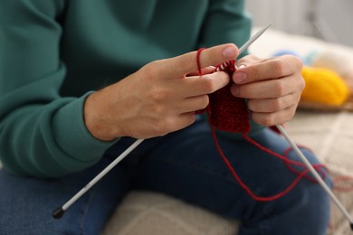 Photo of Man knitting with needles at home, closeup