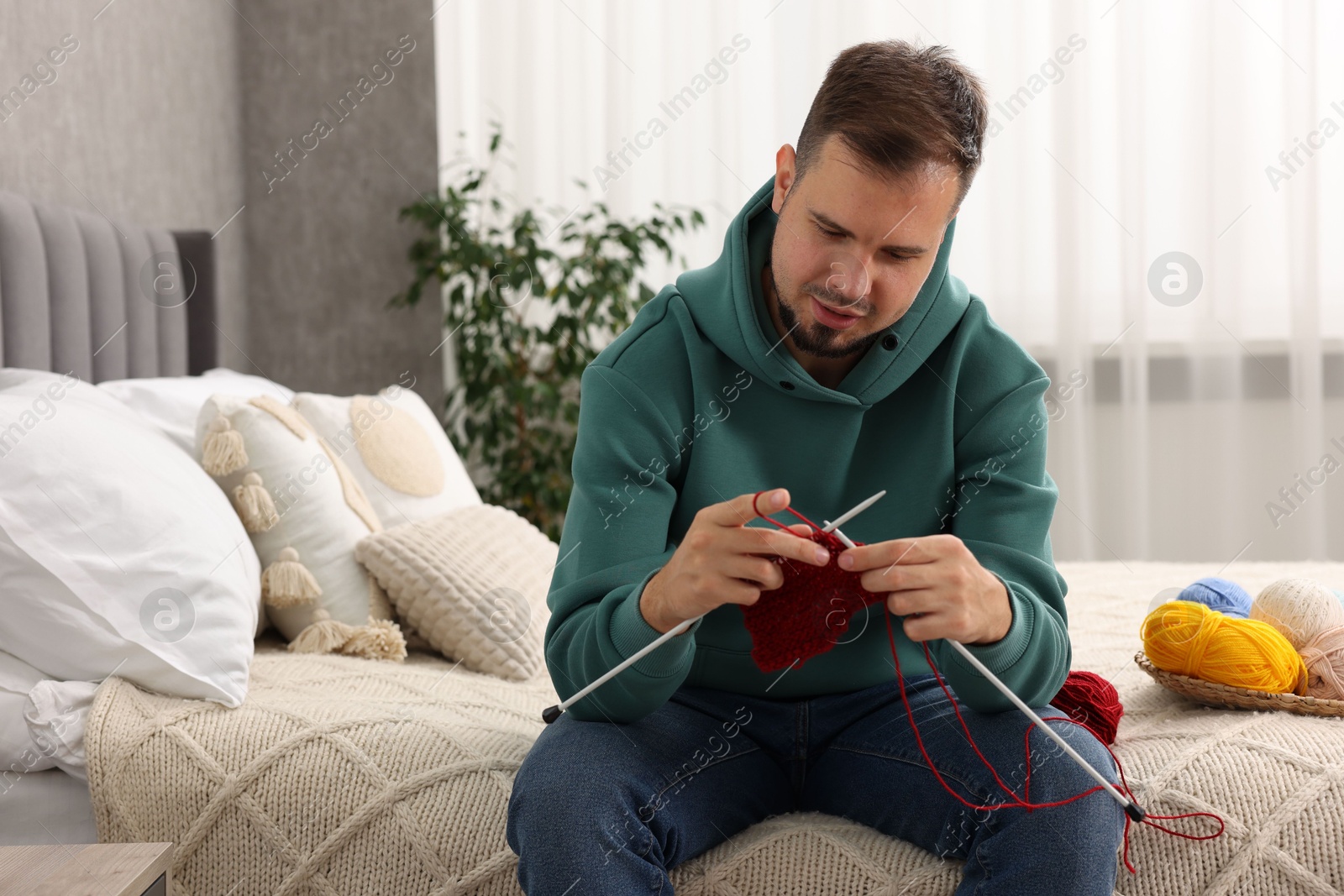 Photo of Man knitting with needles on bed at home