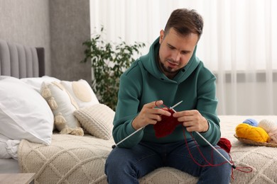 Photo of Man knitting with needles on bed at home