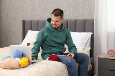 Man learning to knit with online course on bed at home