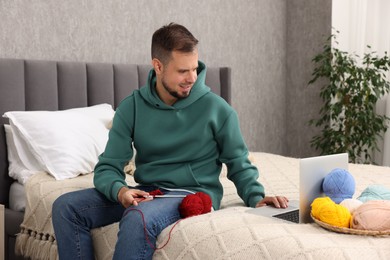 Man learning to knit with online course on bed at home