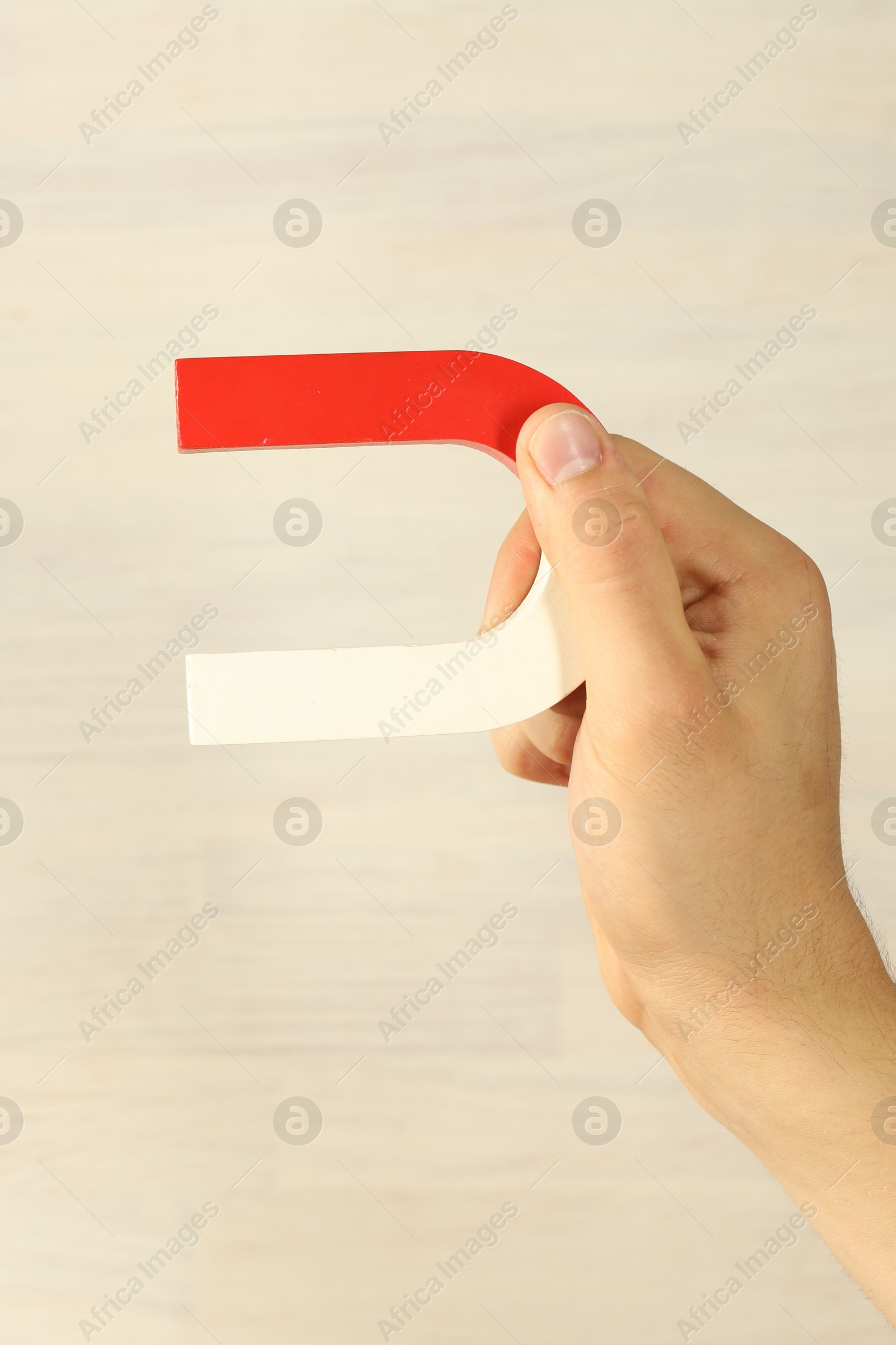 Photo of Man holding horseshoe magnet against light background, closeup