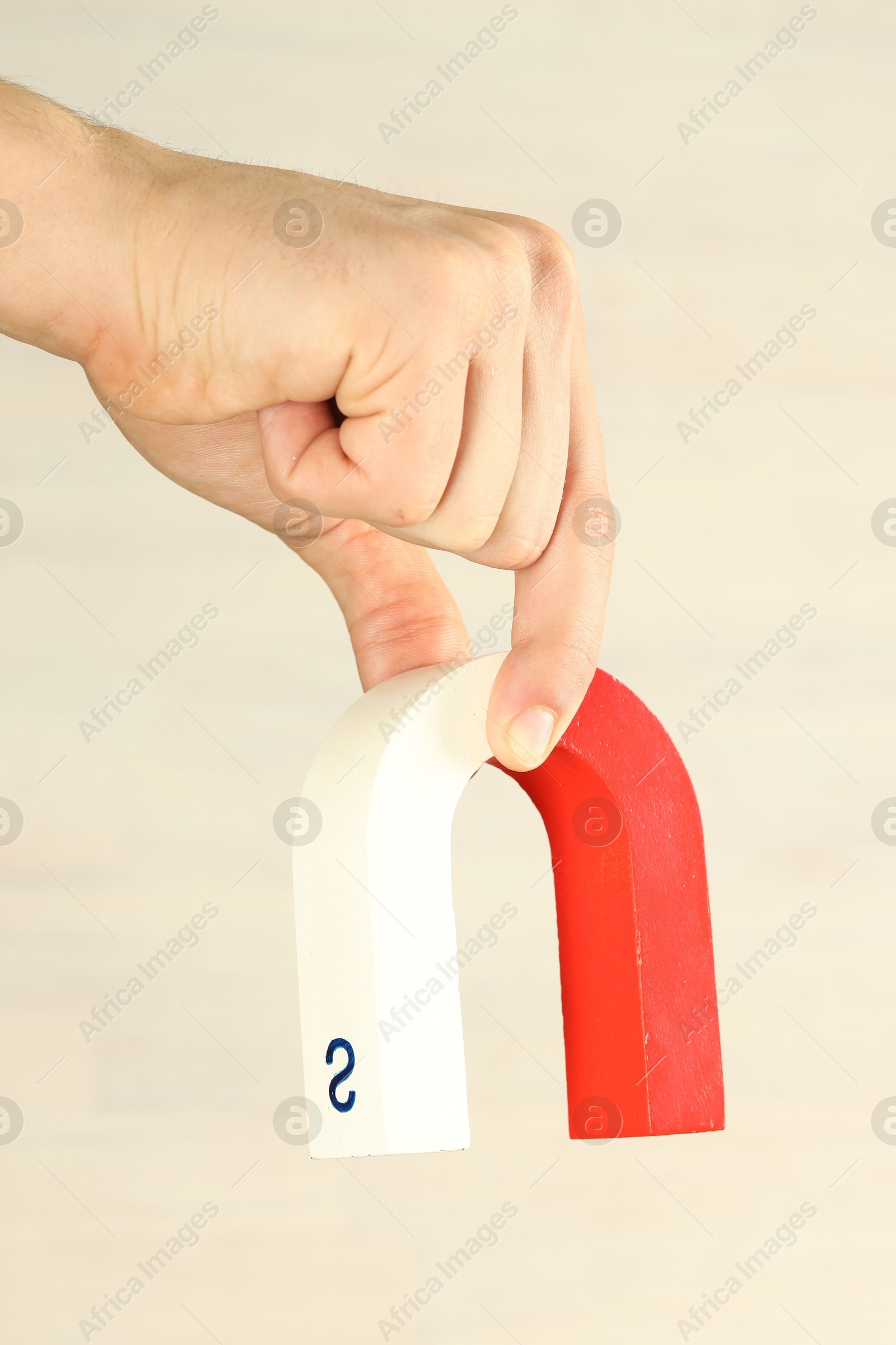 Photo of Man holding horseshoe magnet against light background, closeup