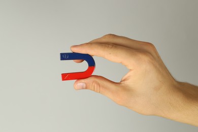 Photo of Man holding horseshoe magnet on grey background, closeup