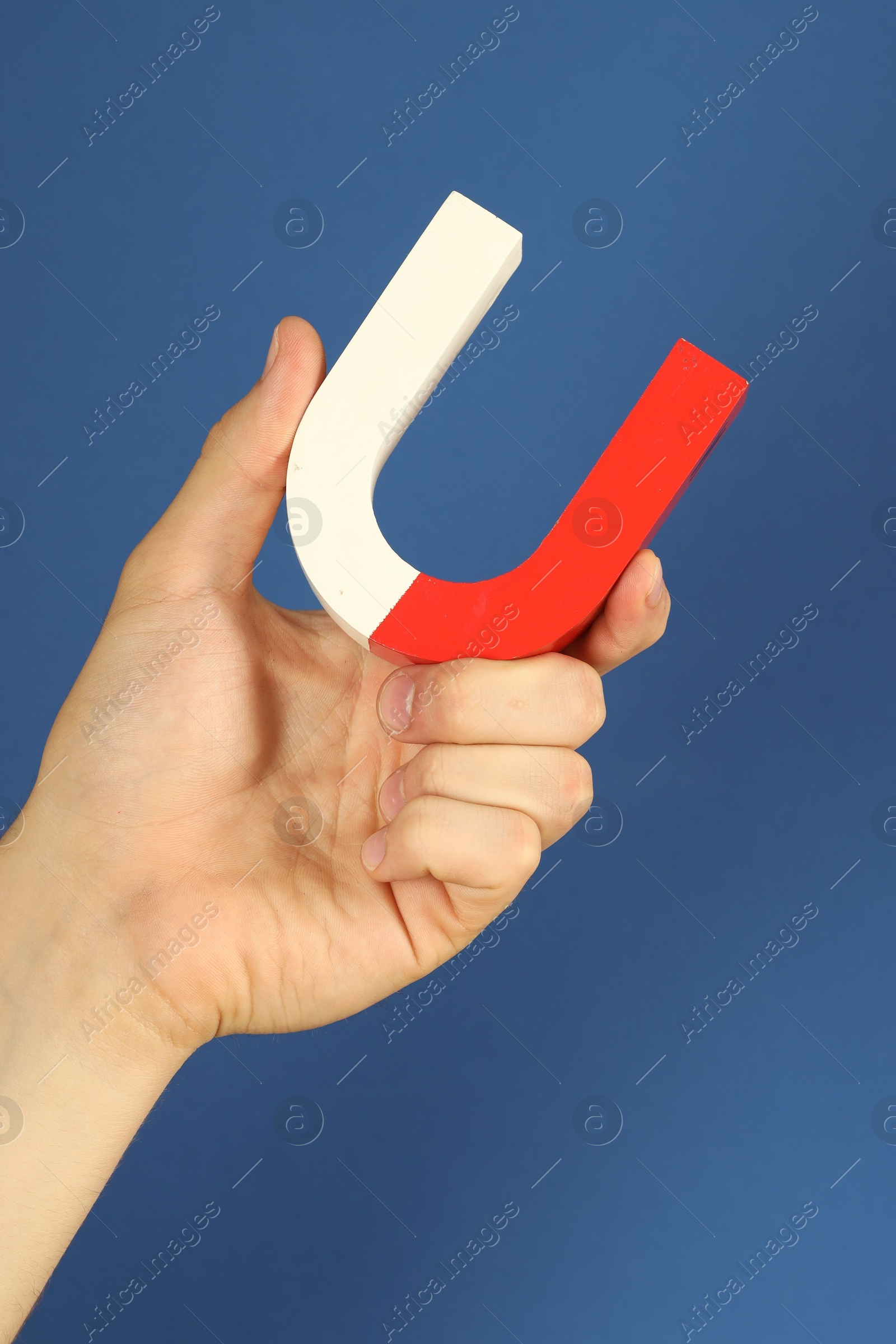 Photo of Man holding horseshoe magnet on blue background, closeup