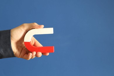 Photo of Man holding horseshoe magnet on blue background, closeup. Space for text