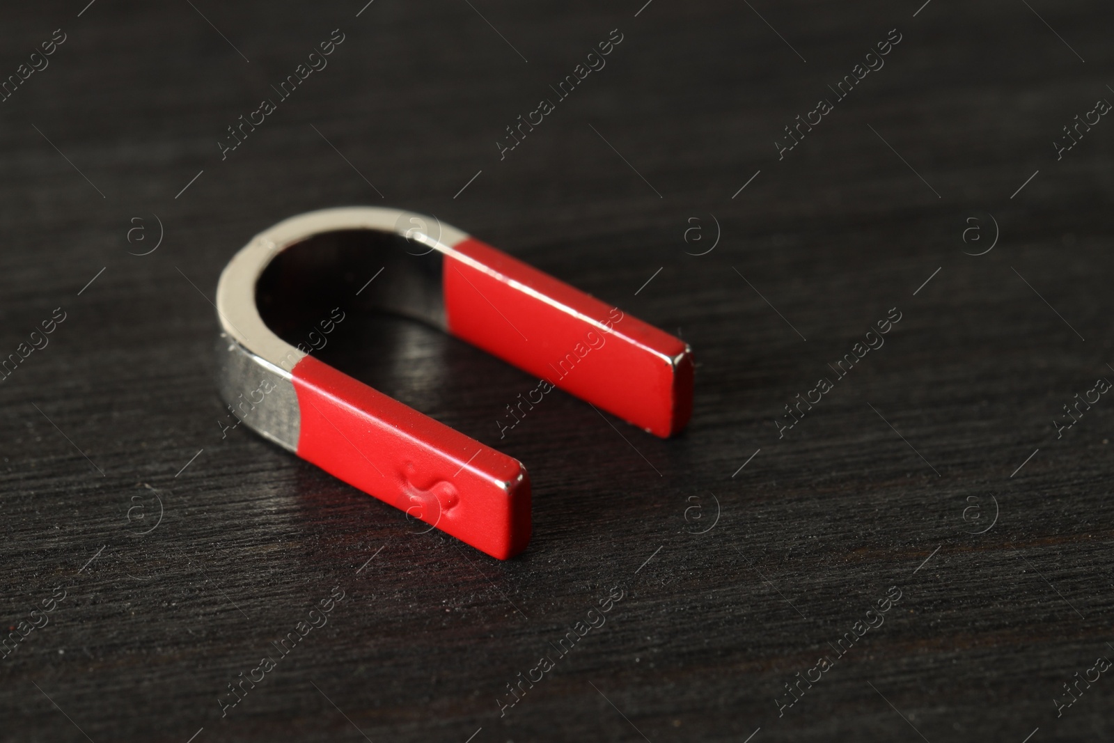 Photo of One horseshoe magnet on black wooden table, closeup. Space for text