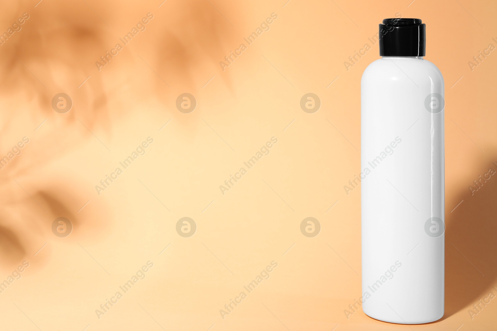 Photo of Shampoo in bottle on pale orange background, space for text