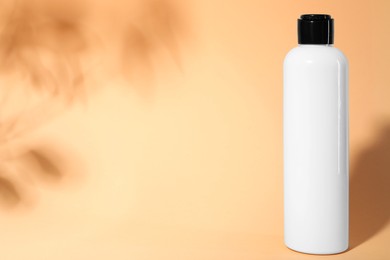 Shampoo in bottle on pale orange background, space for text