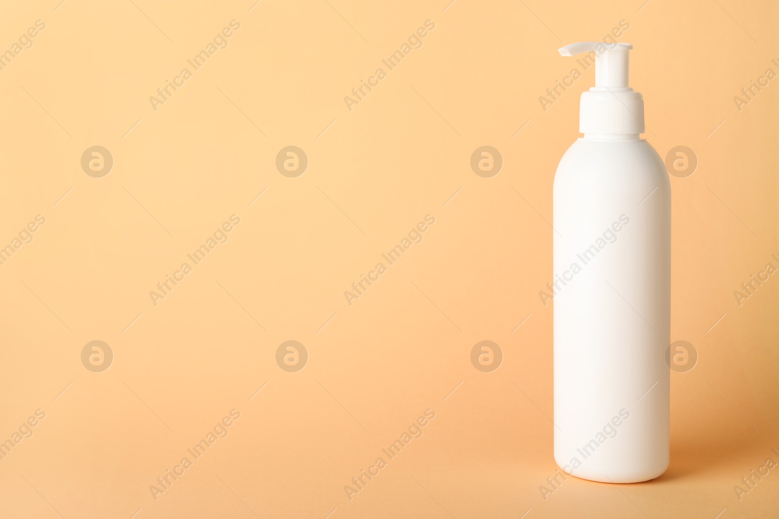 Photo of Shampoo in bottle on pale orange background, space for text