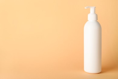 Shampoo in bottle on pale orange background, space for text