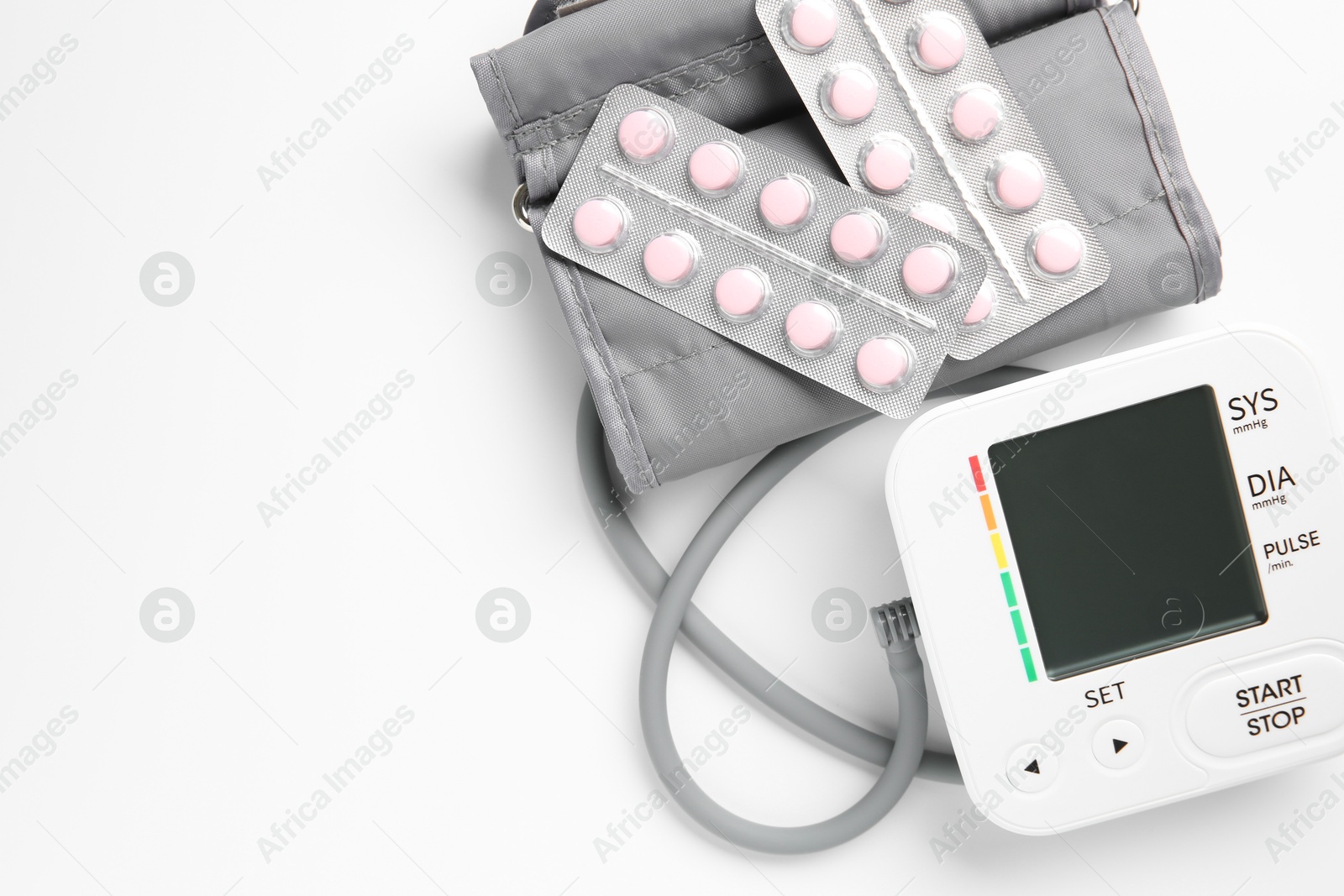 Photo of Blood pressure measuring device and pills on white background, top view. Space for text