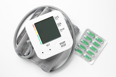 Photo of Blood pressure measuring device and pills on white background, top view