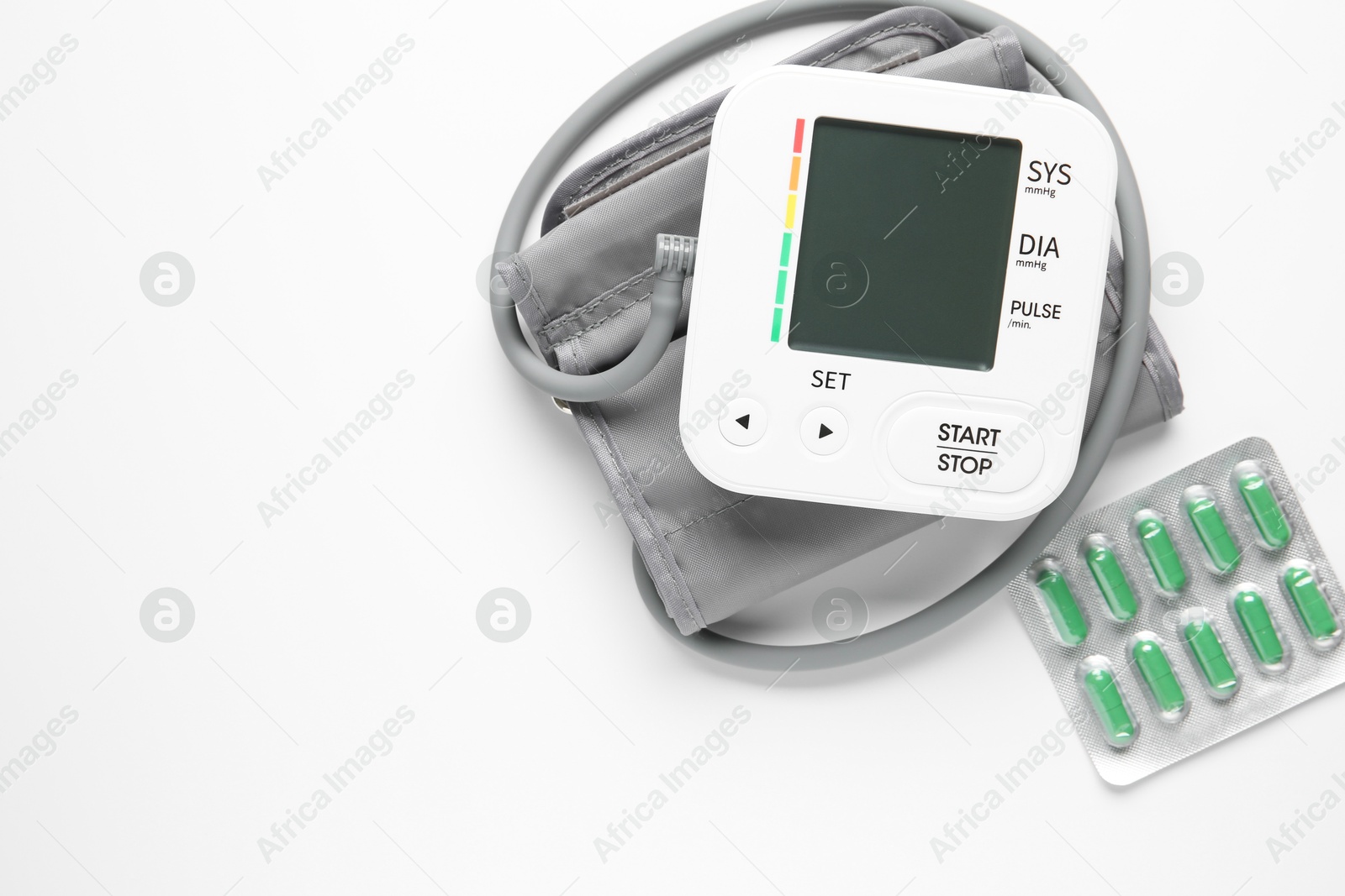 Photo of Blood pressure measuring device and pills on white background, top view. Space for text