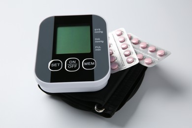 Photo of Blood pressure measuring device and pills on white background, closeup