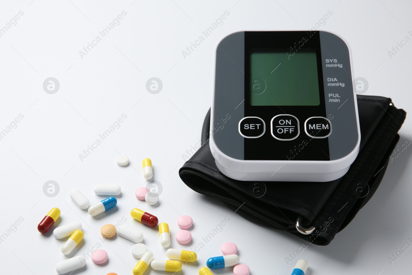 Photo of Blood pressure measuring device and pills on white background, closeup