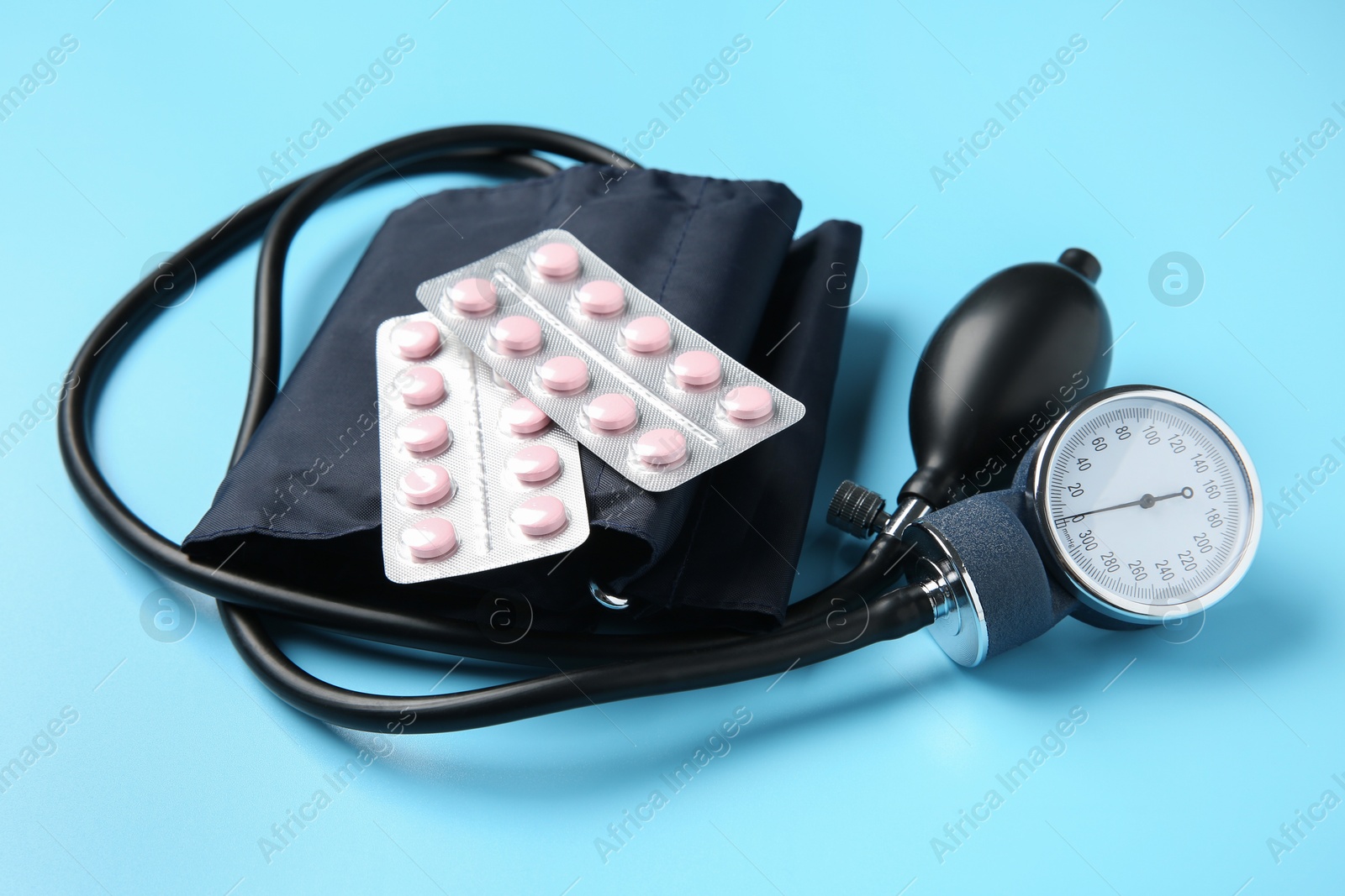 Photo of Blood pressure measuring device and pills on light blue background, closeup