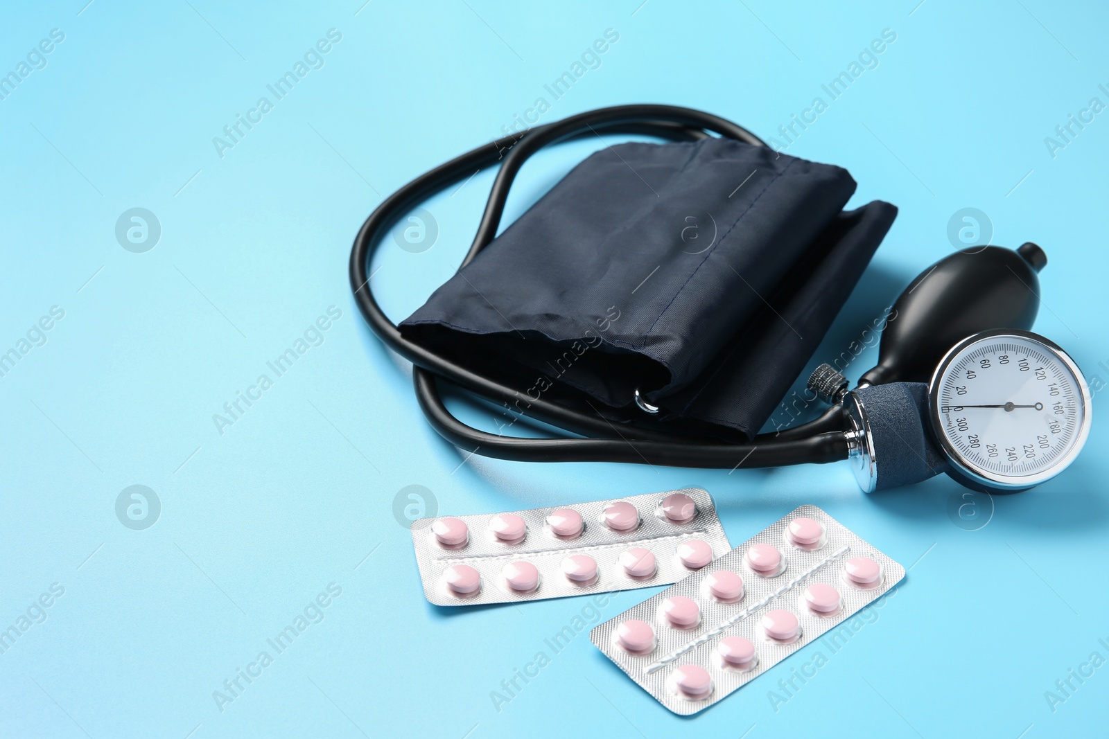 Photo of Blood pressure measuring device and pills on light blue background, space for text