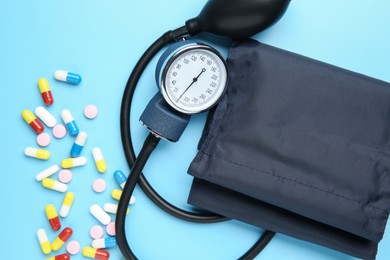 Photo of Blood pressure measuring device and pills on light blue background, top view