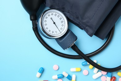 Photo of Blood pressure measuring device and pills on light blue background, top view