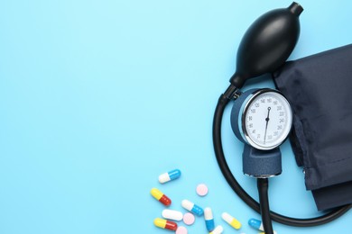 Photo of Blood pressure measuring device and pills on light blue background, top view. Space for text