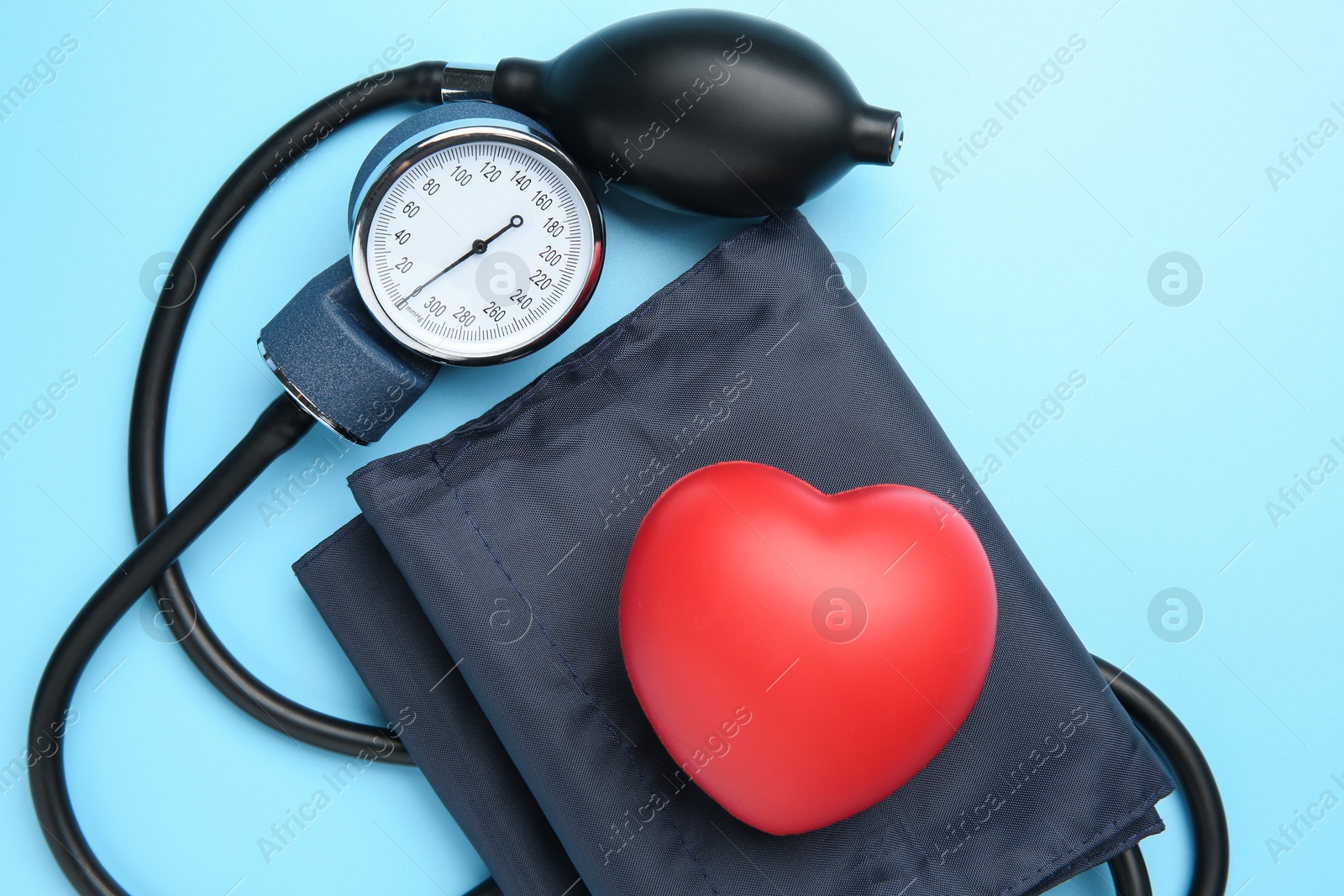 Photo of Blood pressure measuring device and squeeze heart on light blue background, top view