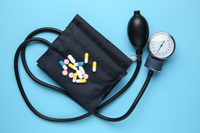 Photo of Blood pressure measuring device and pills on light blue background, top view