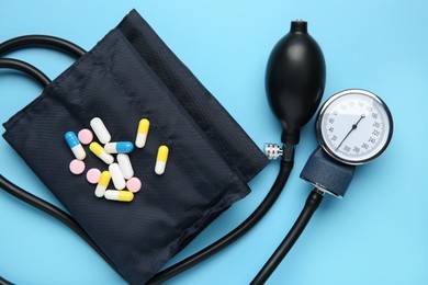 Photo of Blood pressure measuring device and pills on light blue background, top view