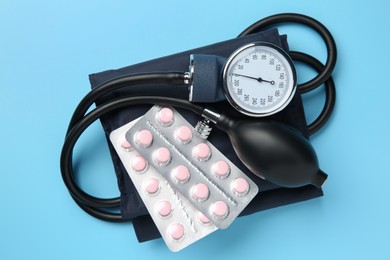 Blood pressure measuring device and pills on light blue background, top view