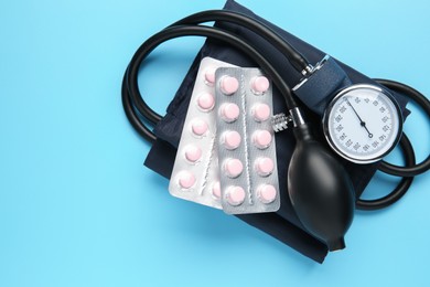 Blood pressure measuring device and pills on light blue background, top view