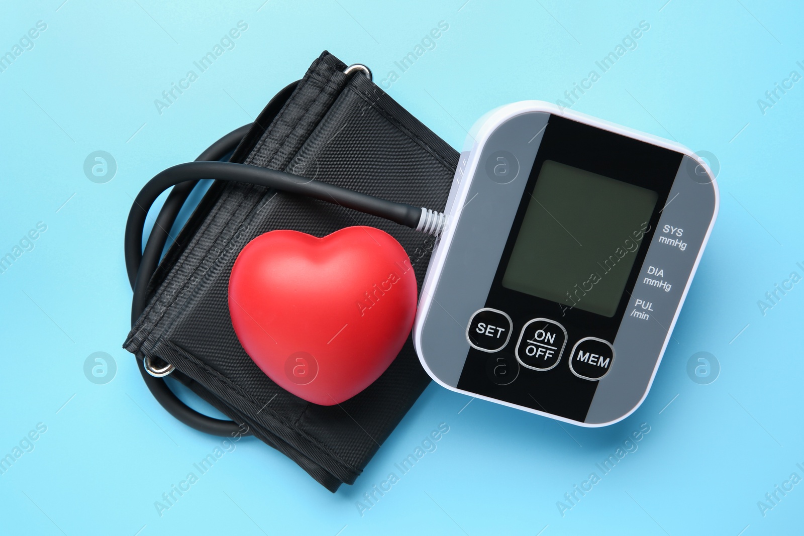 Photo of Blood pressure measuring device and squeeze heart on light blue background, top view