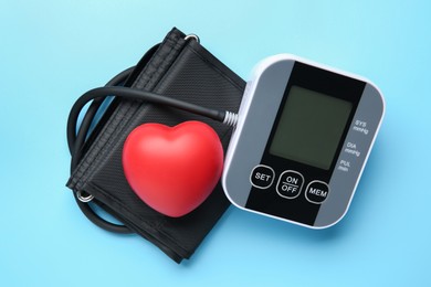 Photo of Blood pressure measuring device and squeeze heart on light blue background, top view