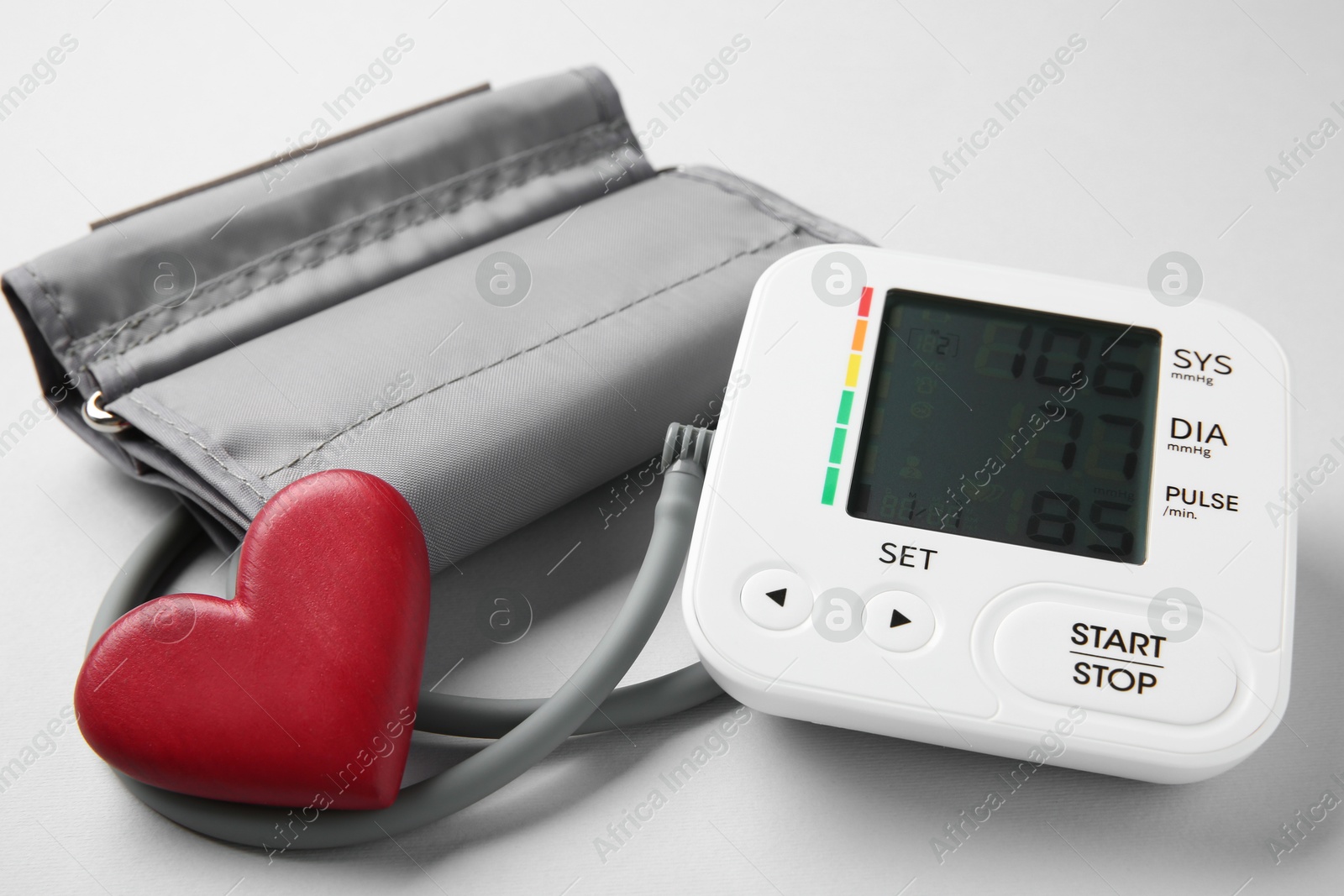 Photo of Blood pressure measuring device and heart figure on light grey background, closeup