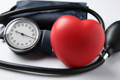 Photo of Blood pressure measuring device and squeeze heart on light grey background, closeup