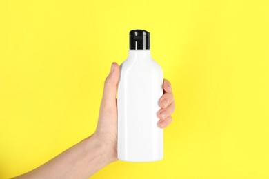 Photo of Woman with shampoo bottle on yellow background, closeup