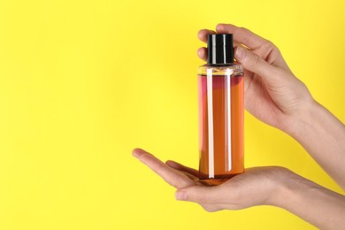 Woman with shampoo bottle on yellow background, closeup. Space for text