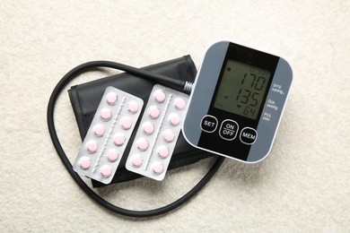 Photo of Blood pressure measuring device and pills on light textured background, top view