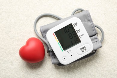 Photo of Blood pressure measuring device and squeeze heart on light textured background, top view