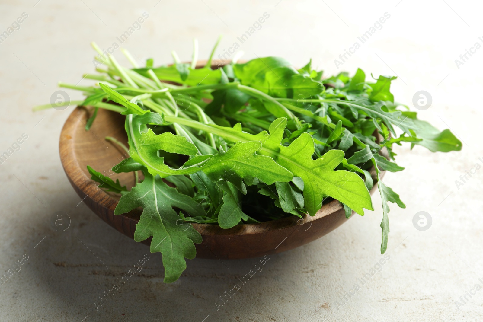 Photo of Many fresh arugula leaves in bowl on grey textured table, closeup